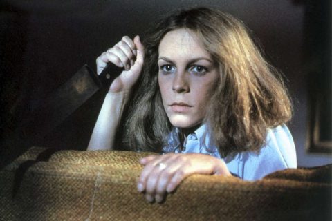 Halloween (1978) screenshot: Laurie crouched behind a sofa holding a knife.